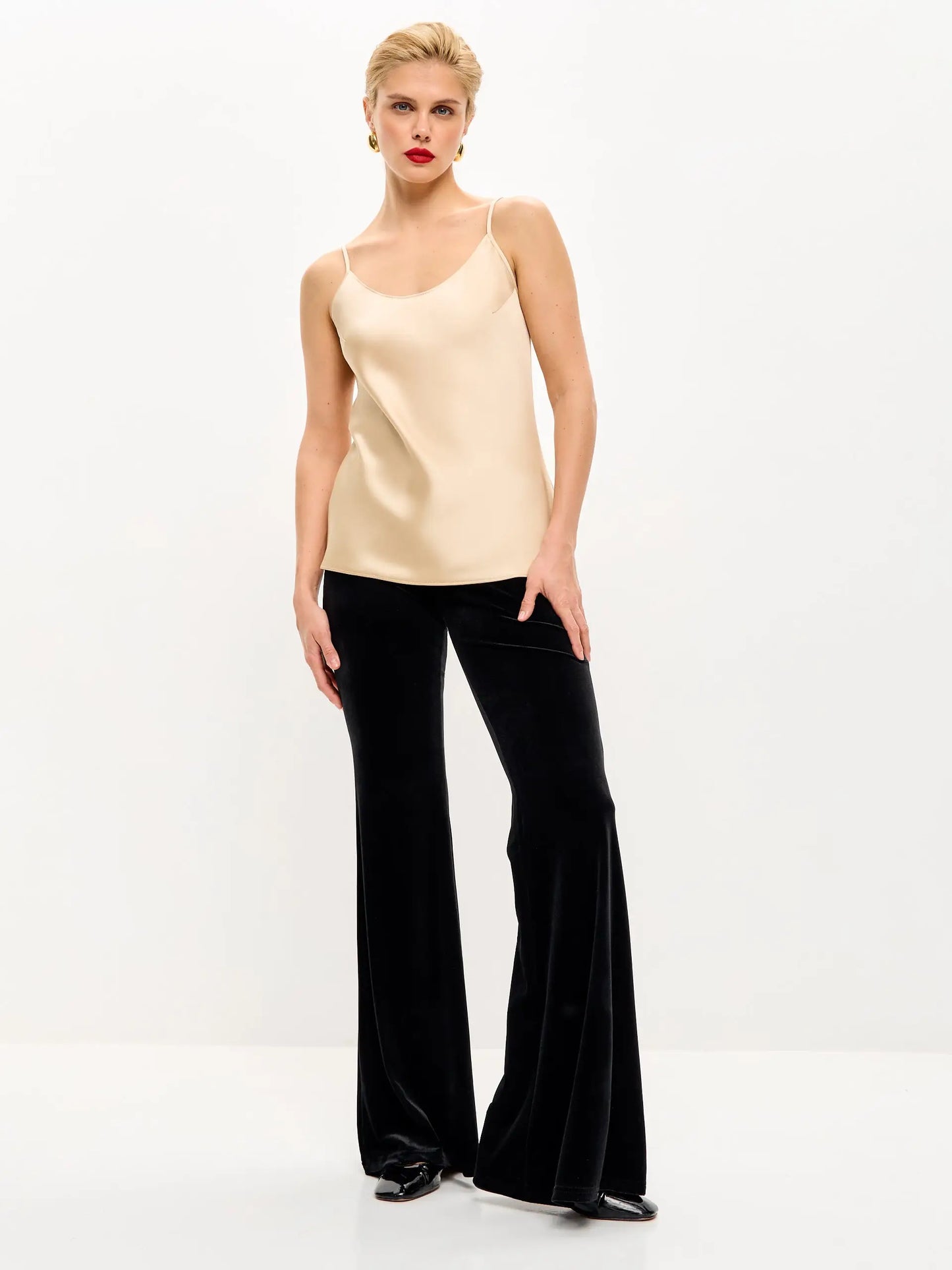 Woman in a beige camisole and black velvet bell-bottom pants.